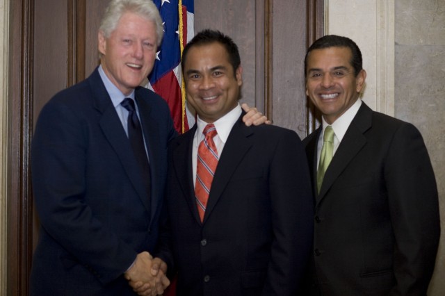 President Bill Clinton on the left, in front of an American flag, shaking hands with Romel Pascual, with Mayor Antonio Villaraigosa standing off to the right